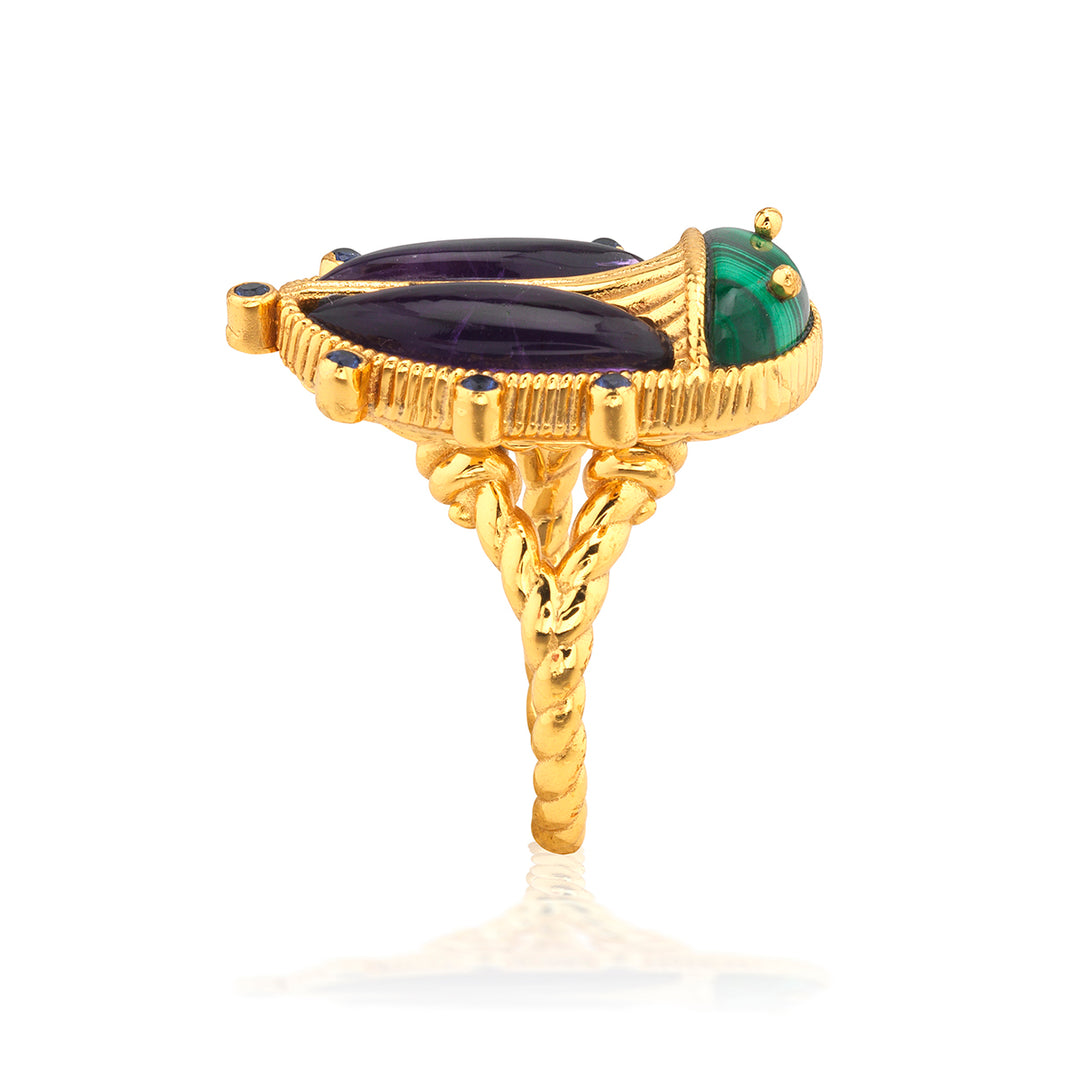 Gold beetle ring with green and black gemstones on a white background