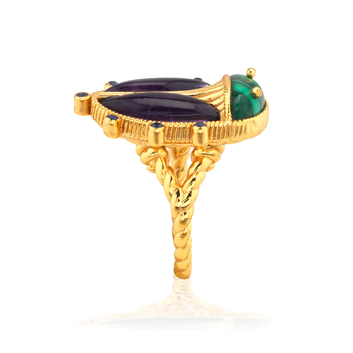 Gold beetle ring with green and black gemstones on a white background