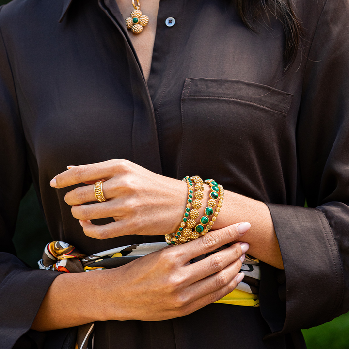Close-up of a person wearing multiple gold and green bracelets 