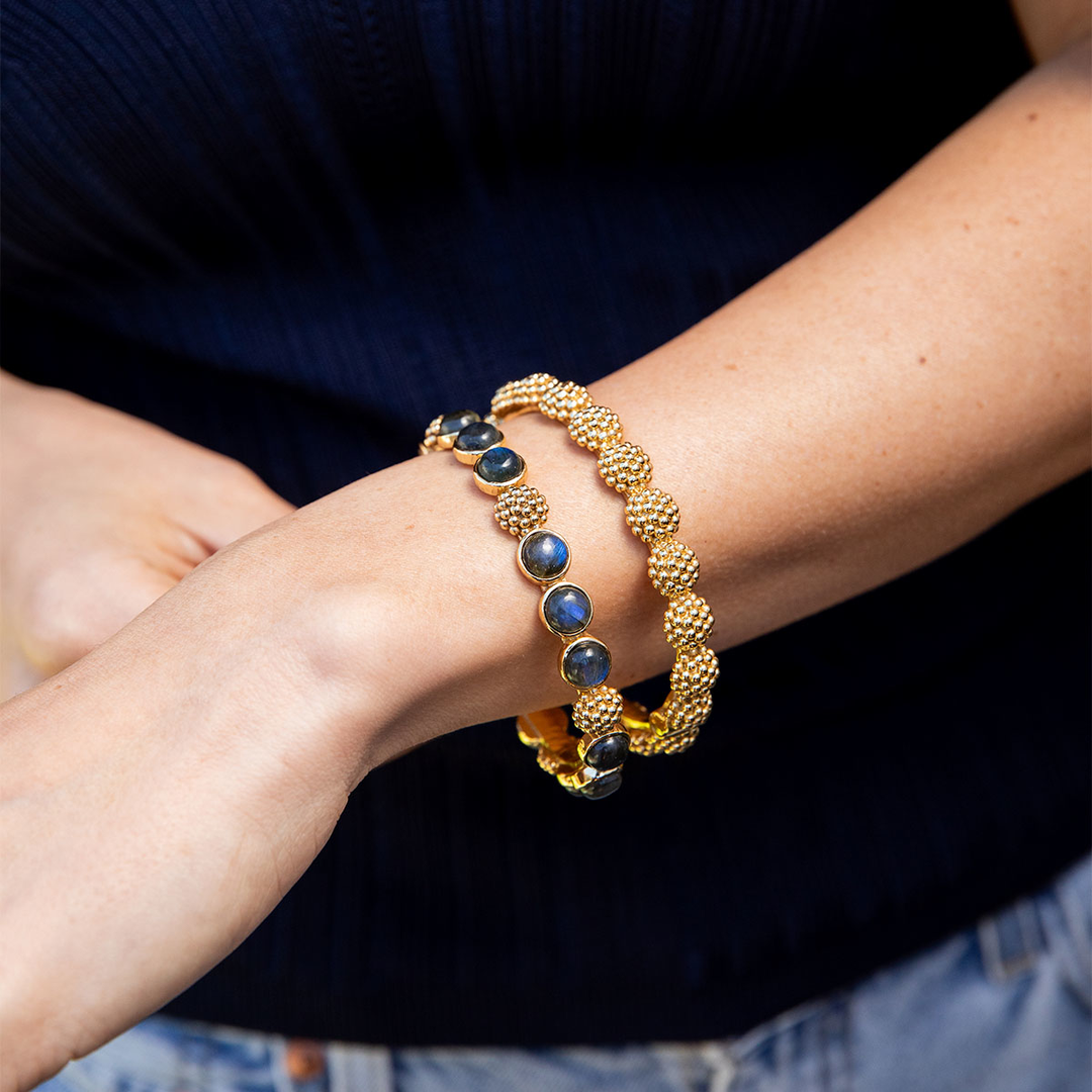 Gold bracelet with blue labradorite stones on a person's wrist against a dark background