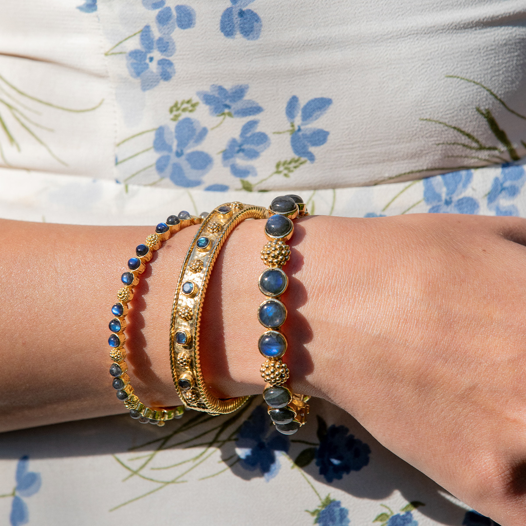 A person wearing a selection of gold and labradorite bracelets with a berry motif on each one