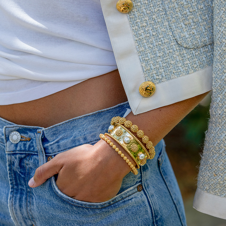 Close-up of a person wearing gold berry and pearl bracelets on a blurred background