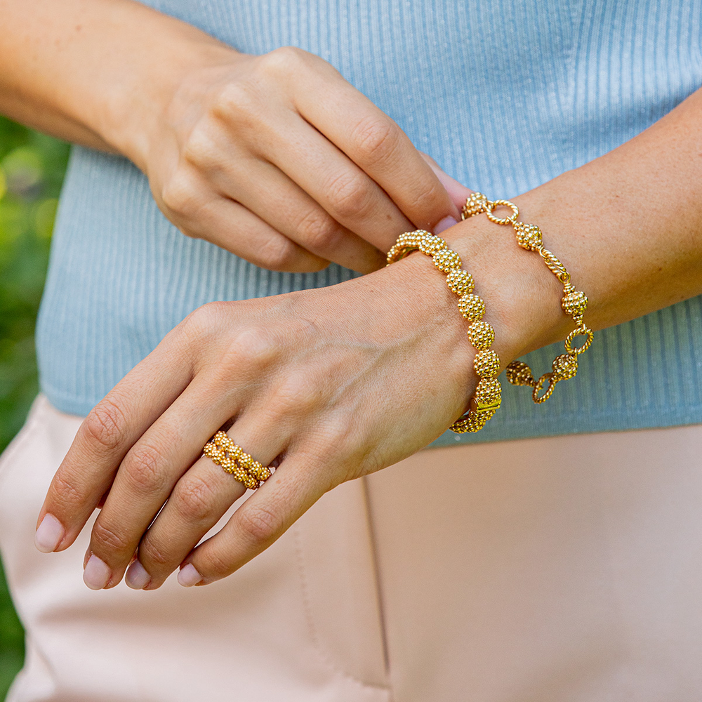 A person wearing two bracelets and a ring with similar bramble berry designs 
