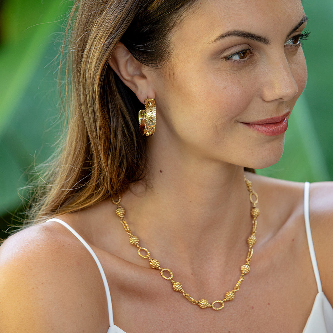 Woman wearing gold berry and thread jewelry with a green blurred background