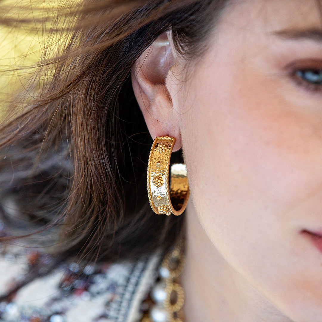 Close-up of a person wearing a gold berry and thread hoop earring with a blurred background