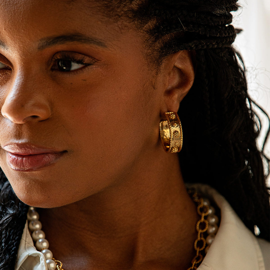 Close-up of a woman wearing gold berry and thread hoop earrings and a pearl necklace