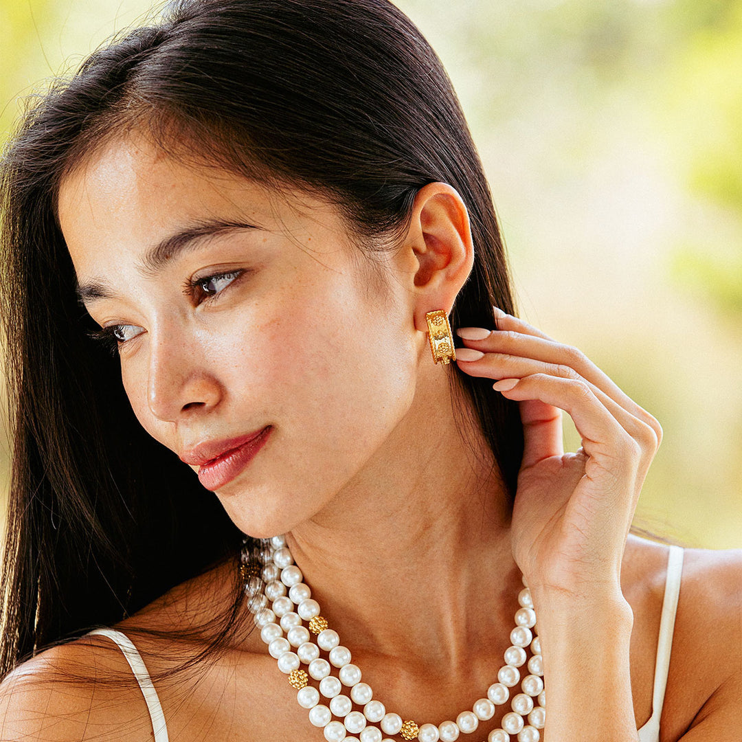 Woman wearing gold earrings and a pearl necklace with a blurred outdoor background