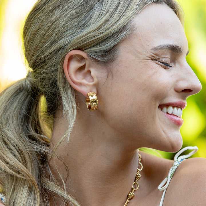 Close-up of a woman wearing gold hoop earrings with a blurred green background