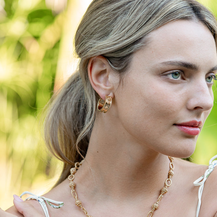 Woman wearing gold hoop earrings and necklace with a blurred green background
