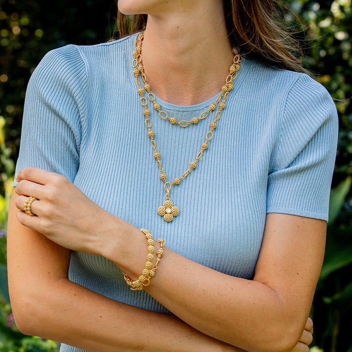 Woman wearing gold necklaces and bracelet with a blurred green background