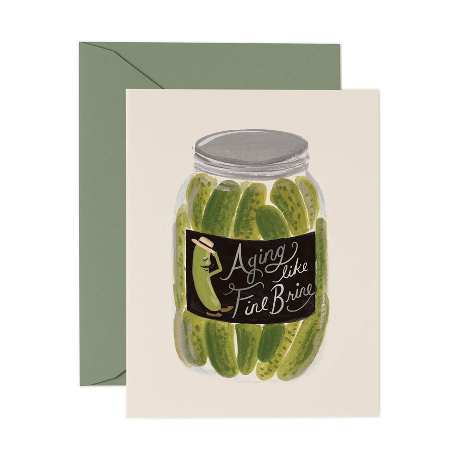A card with an illustration of a jar of pickles, the label reading "aging like fine brine" sitting on top of a pine green envelope