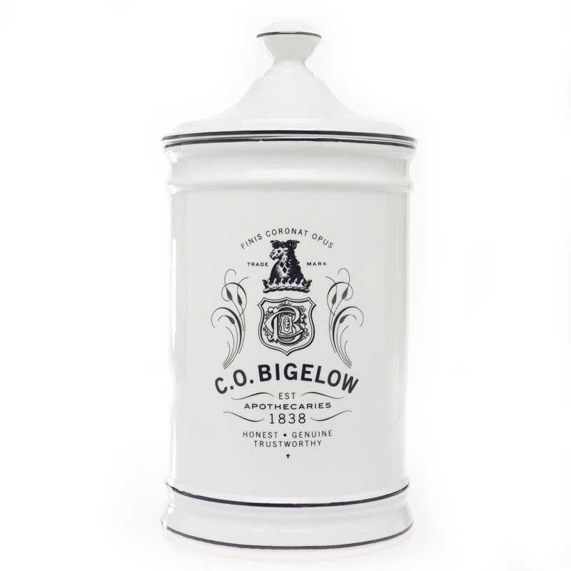 Tall white CO Bigelow lidded container with black text reading "finis coronat opus, trademark CO Bigelow Apothecaries est 1838" 