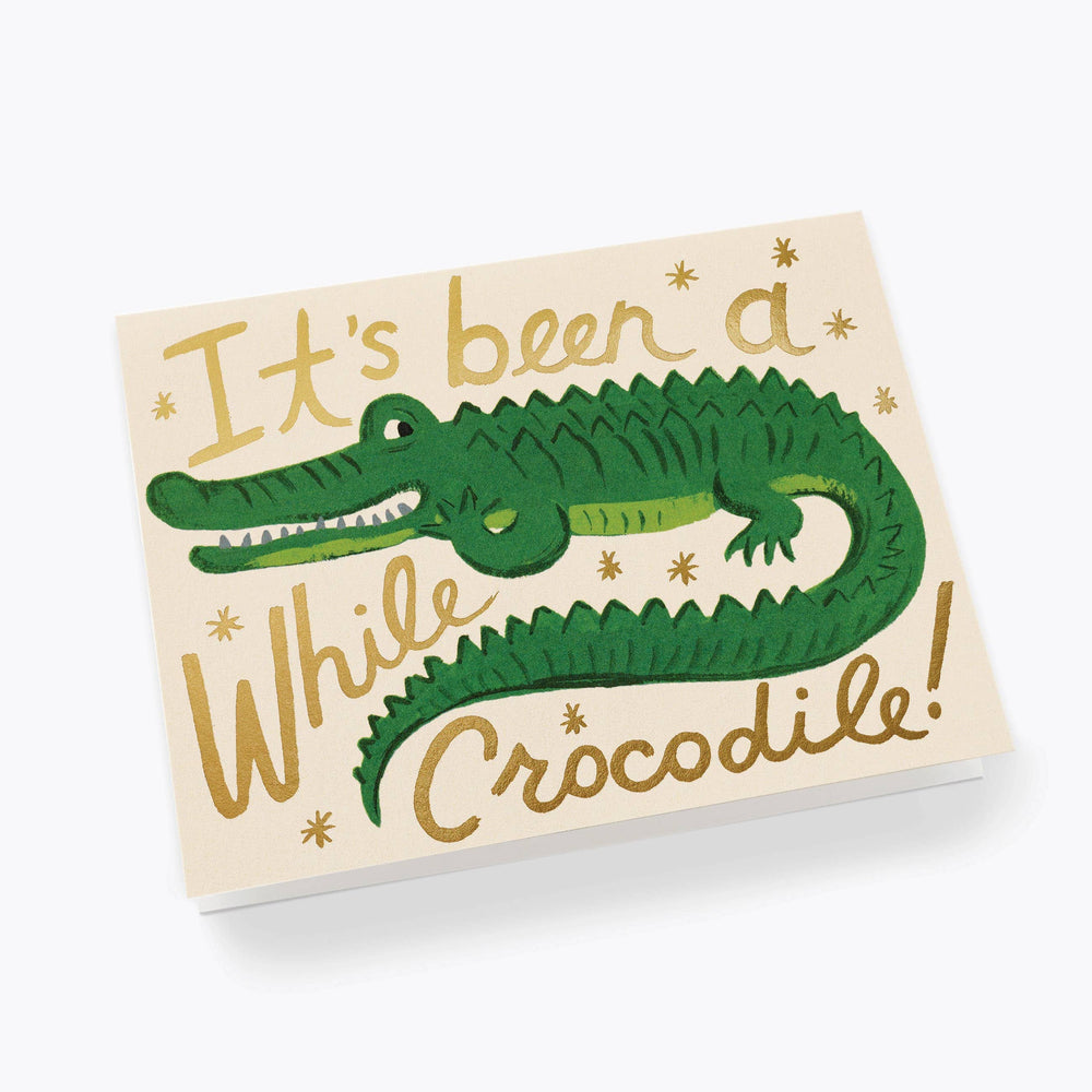 Card with green crocodile illustration and text 'It's been a while crocodile' on ivory paper