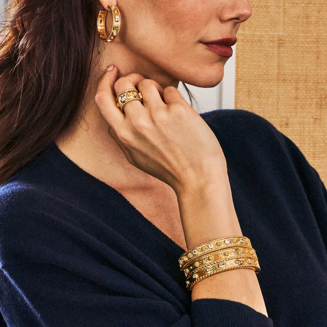 Woman wearing gold berry and thread jewelry including earrings, ring, and bracelet against a neutral background