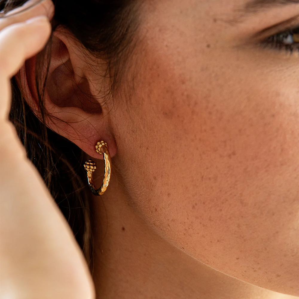 A close up of a woman wearing berry design gold earrings