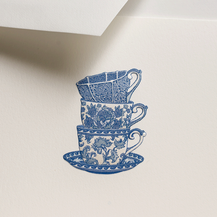 a close up of a stationery notecard with a stack of blue and white delft chinoiserie teacups on a beige background