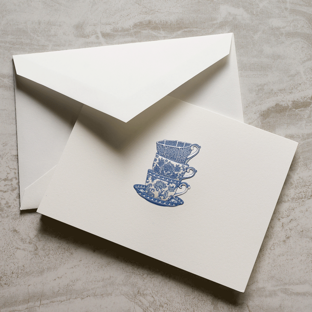 White card with blue delft chinoiserie cup design engraved and matching envelope on a gray surface