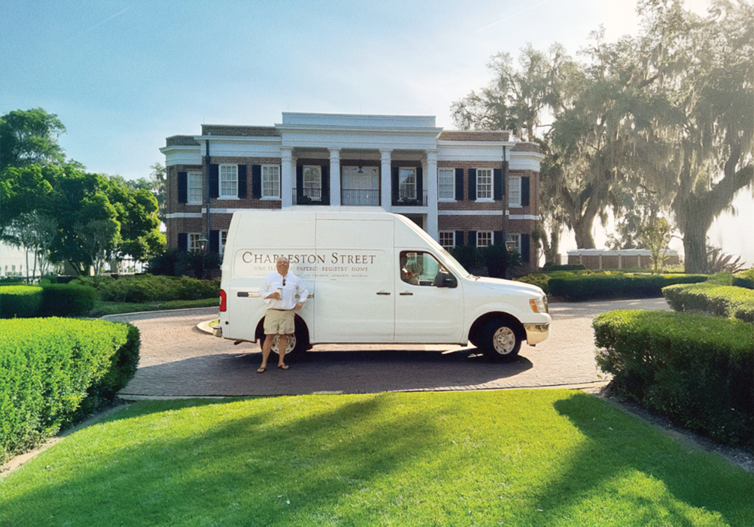 A  flower delivery truck with Charleston Street branding on the side in front of a large brick house while the owner of Charleston Street stands in the foreground