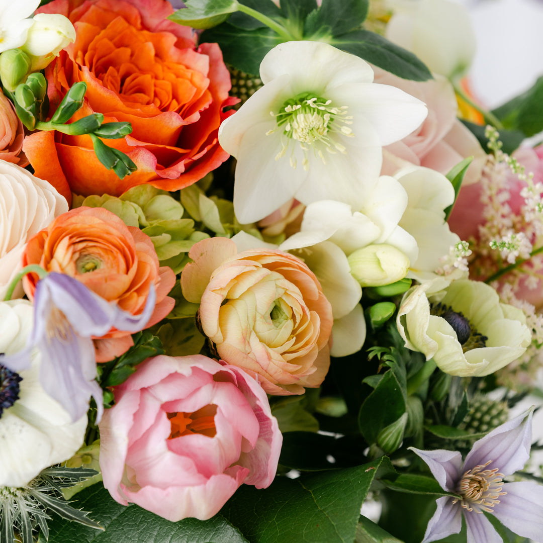 Bouquet of colorful flowers including roses, ranunculus, anemone, and lisianthus and hydrangeas with green leaves.
