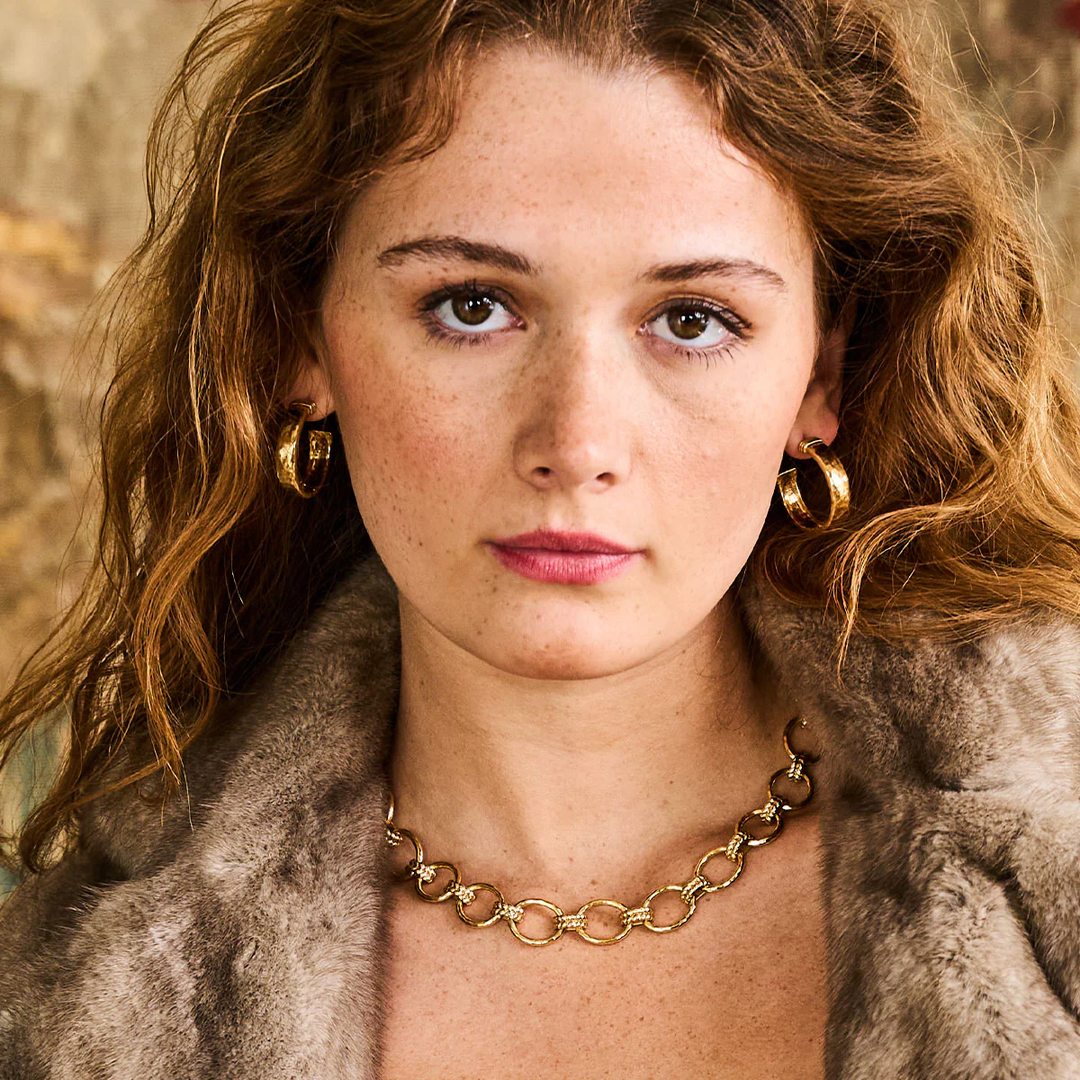 Woman wearing gold earrings and a gold chain necklace with a fur coat.
