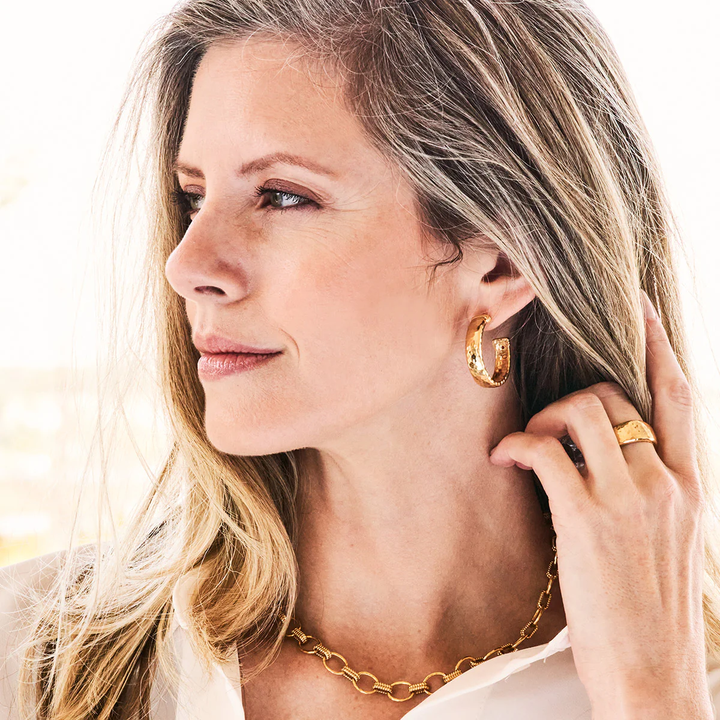 Woman wearing gold hoop earrings and a gold chain necklace, with a blurred background.