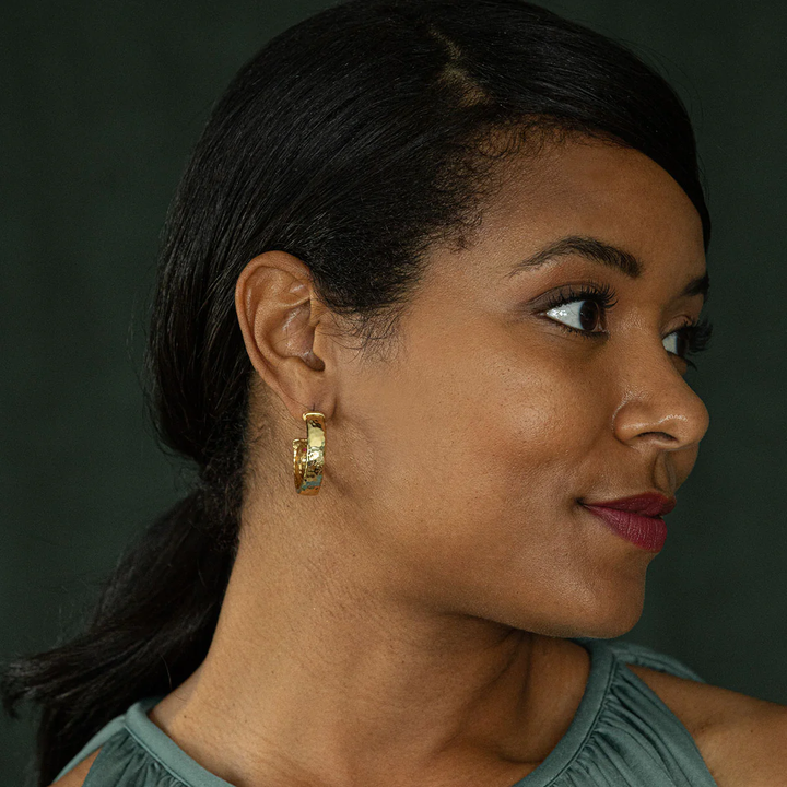 Woman wearing gold hoop earrings against a dark background