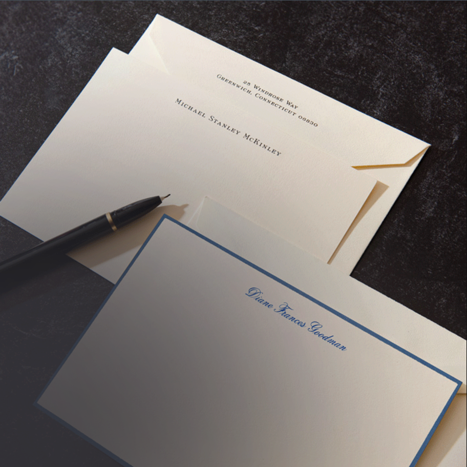 Two Crane and Co stationery items with engraved names on a dark surface