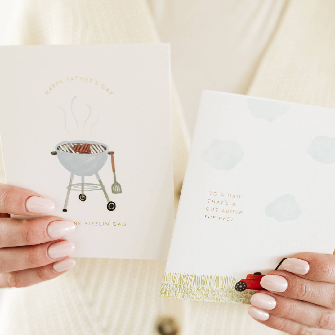 Two fathers day grill themed greeting cards held by hands with a decorative border and text.