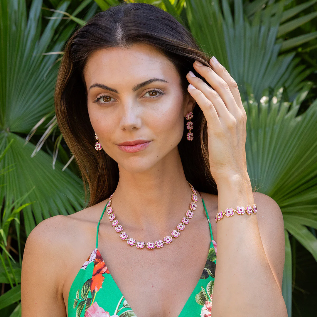 Woman wearing pink floral gold jewelry with a green leafy background