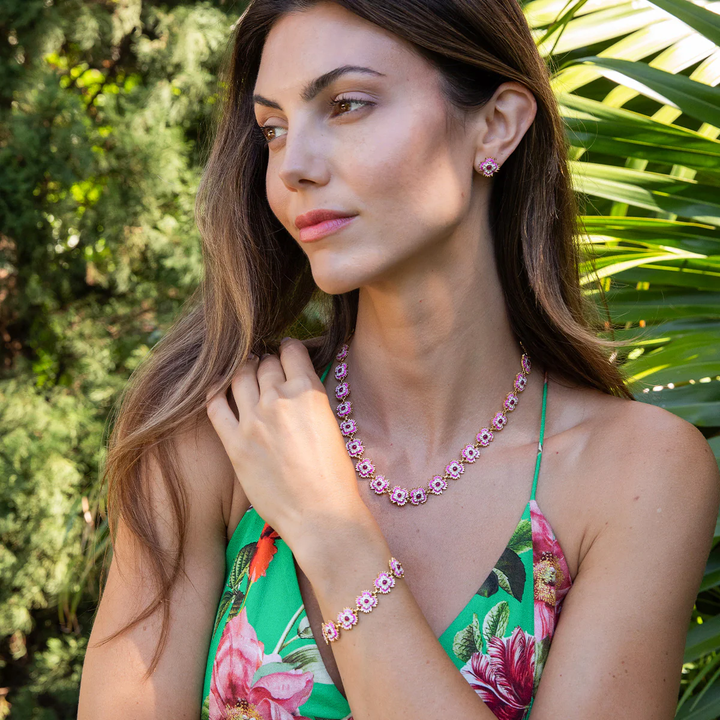 Woman wearing a floral dress and pink jewelry with greenery in the background
