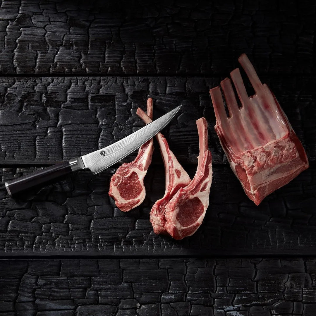 Raw lamb chops and a boning knife on a textured black surface