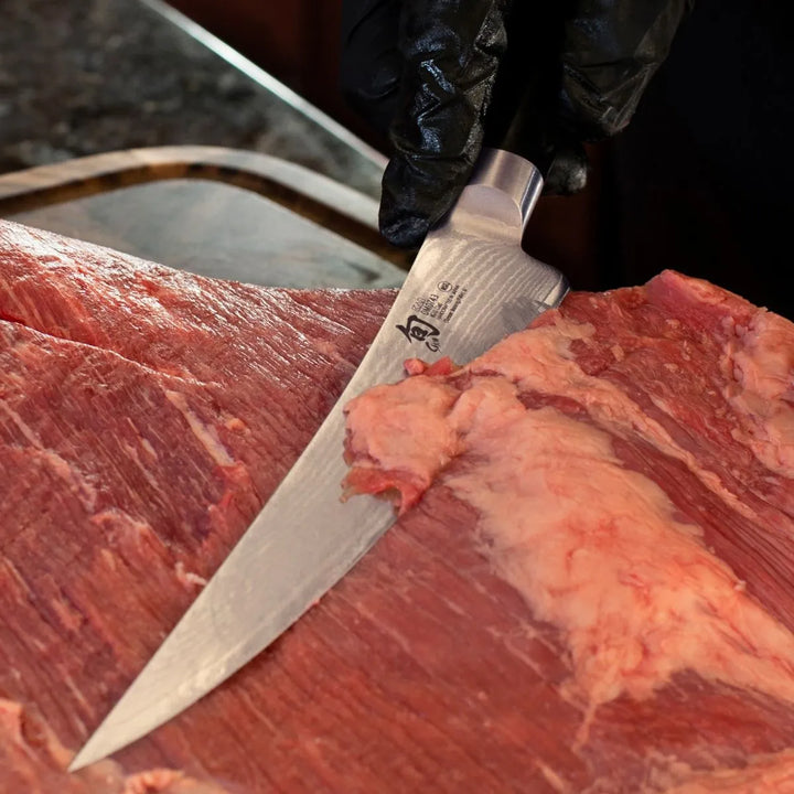 Boning knife cutting into a piece of raw meat on a dark surface