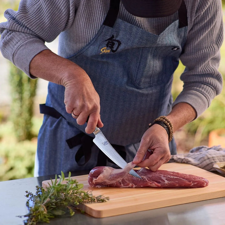 Person in a kitchen setting, preparing meat on a cutting board with a blurred background