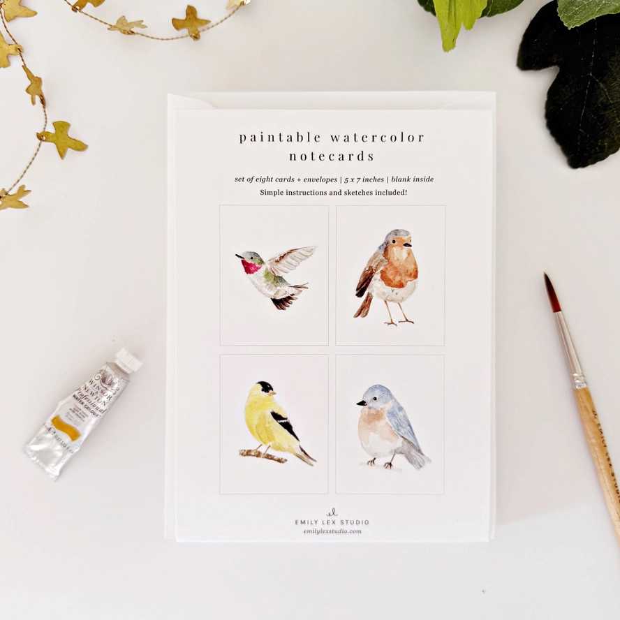 A paintable watercolor book with bird illustrations with a brush and paint bottle.