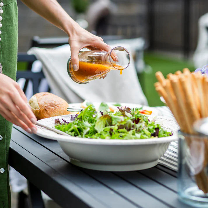Person pouring dressing over a salad in a white bowl with a lace design