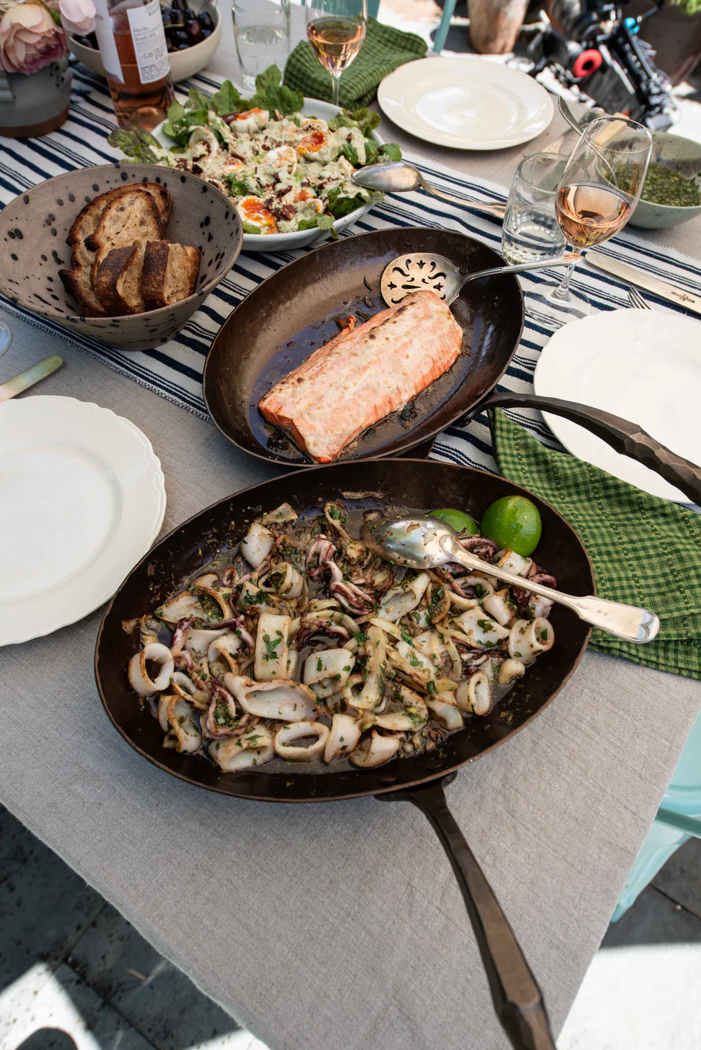 Dining table with pans of food, plates, and glasses on a gray tablecloth.