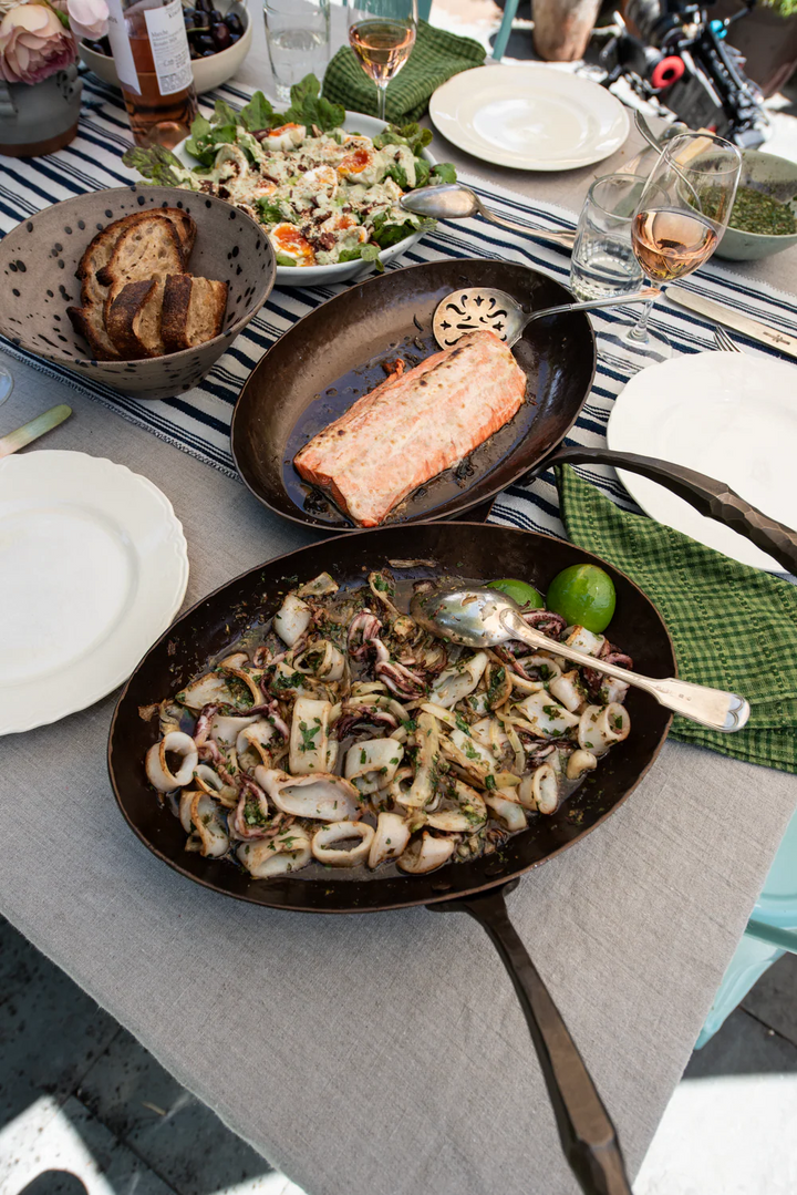 Dining table with pans of food, plates, and glasses on a gray tablecloth.