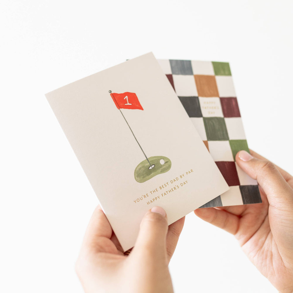Two greeting cards held by hands, one with a golf design and the other with a checkered pattern.