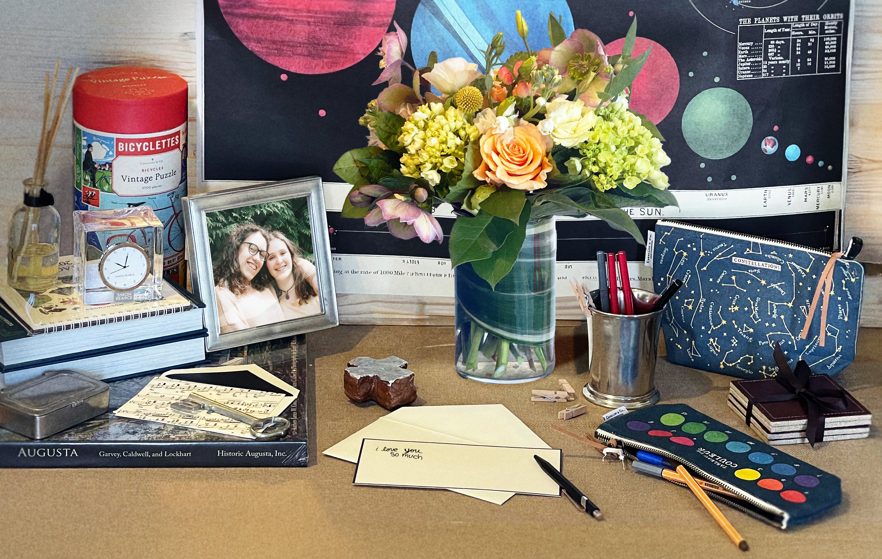 Desk with books, photos, flowers, and stationery items on a wooden surface.