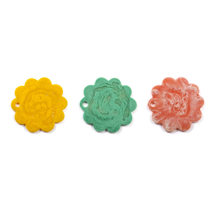 Three small flower-shaped jewelry charms or beads in yellow, mint green, and coral pink, arranged horizontally on a plain white background.