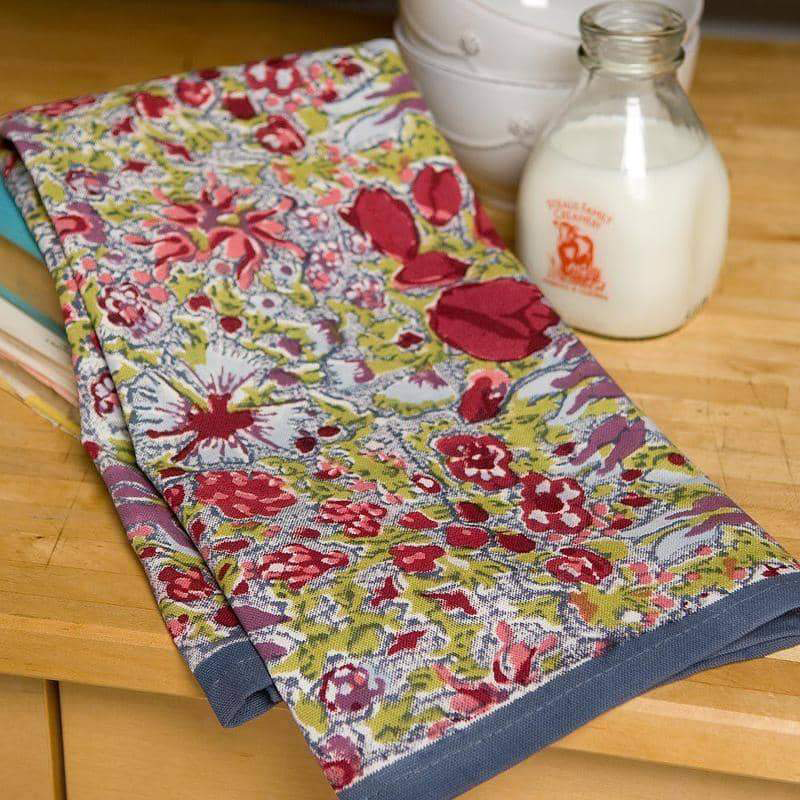 Floral-patterned tea towel on a wooden surface with a bottle of milk in the background