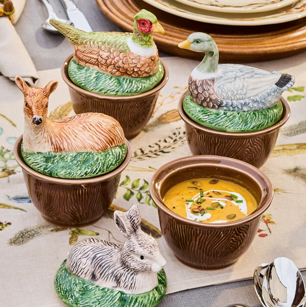 Set of animal-shaped ceramic bowls on a table; one without a lid revealing soup