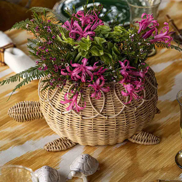 Decorative turtle-shaped planter with pink flowers on a tablecloth