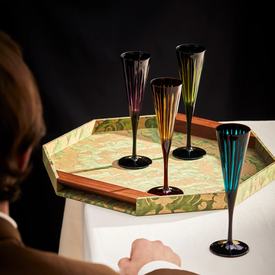 Colorful glass champagne flutes on a decorative tray with a person partially visible.