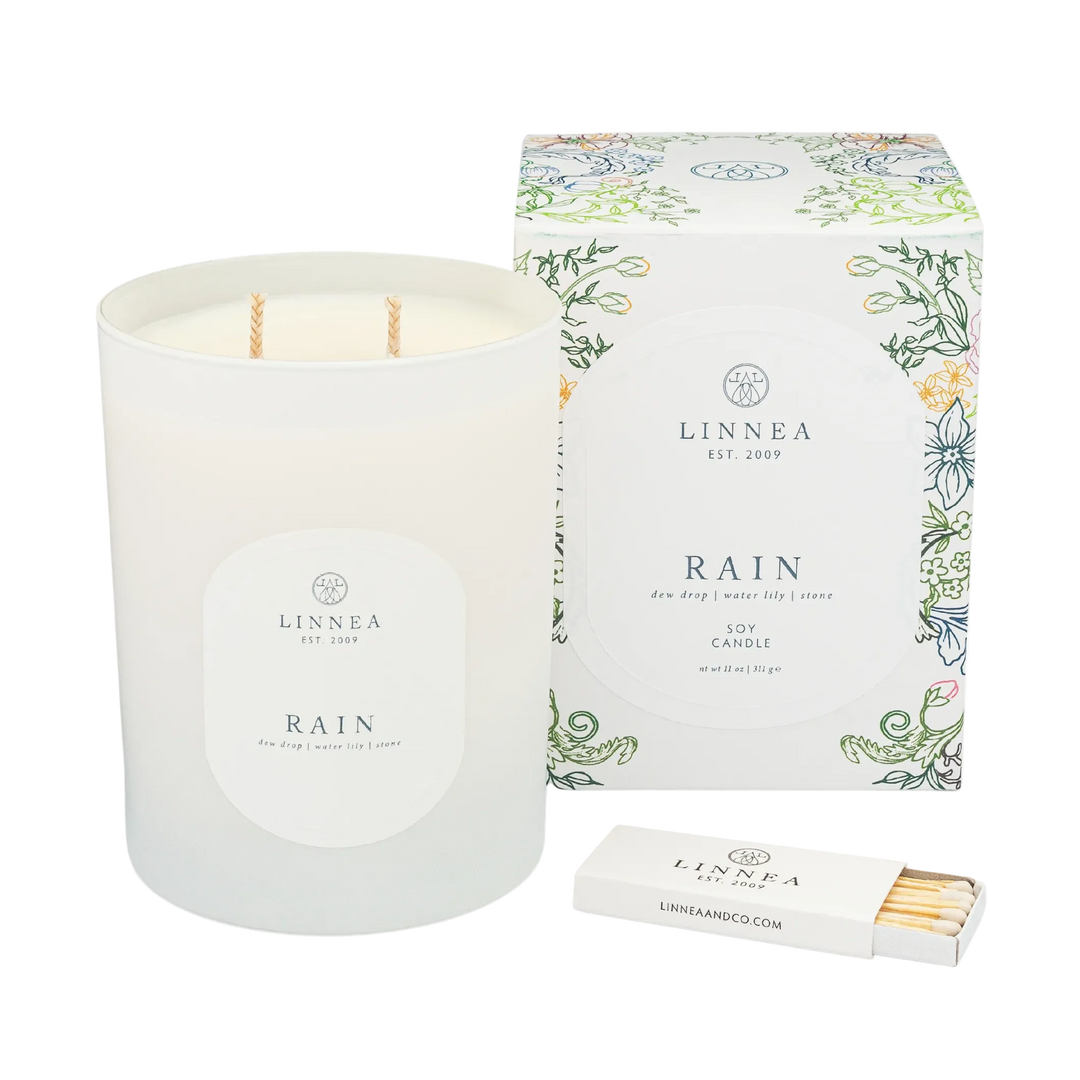 A linnea two wick rain scented candle next to its packaging and a box of matches