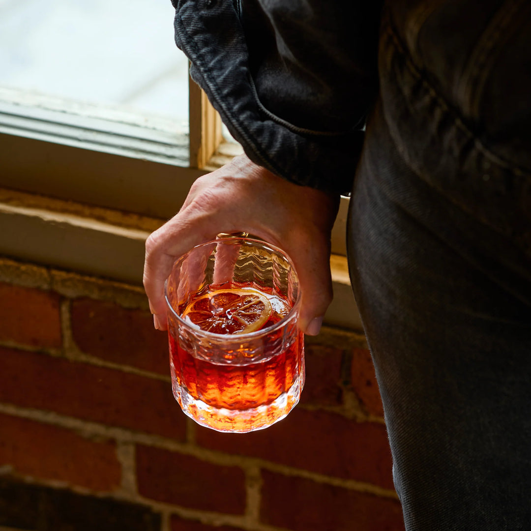 Hand holding a glass of red liquid against a brick wall