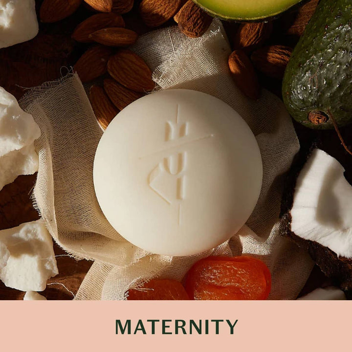 White soap bar with branding surrounded by natural ingredients on a pink background with 'MATERNITY' text.