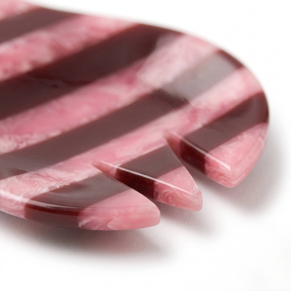A close-up of a pink and dark burgundy striped hair tool, likely a comb or styling brush, on a white background.