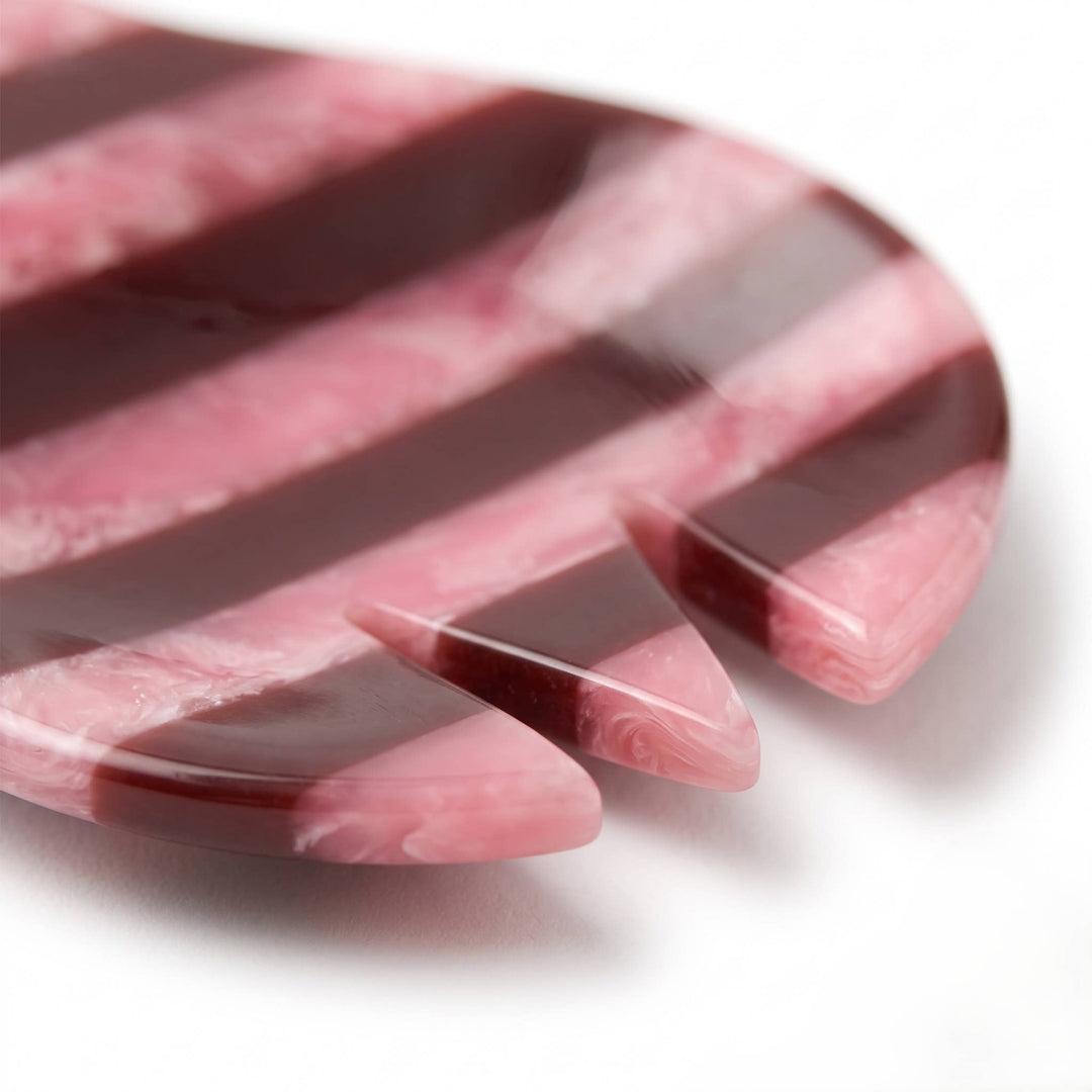 A close-up of a pink and dark burgundy striped hair tool, likely a comb or styling brush, on a white background.