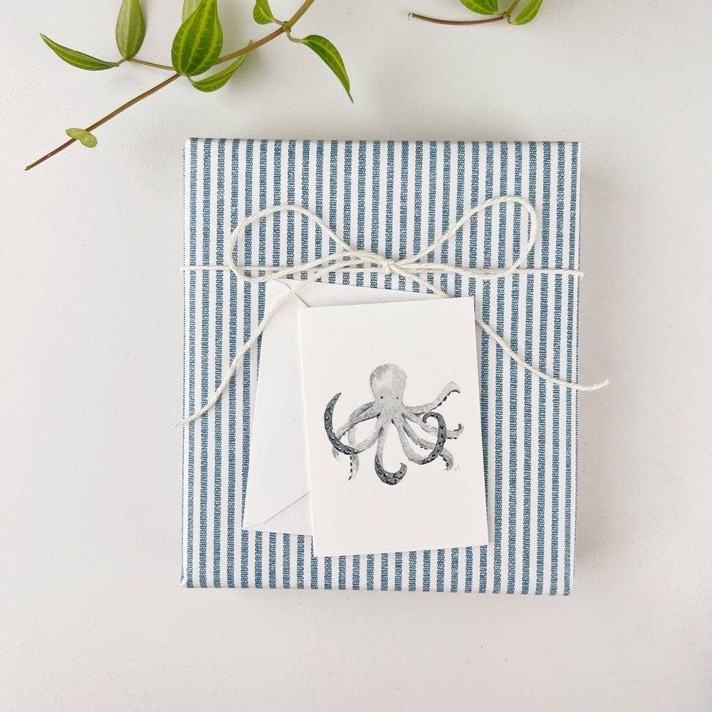 Gift box with blue and white striped paper and a white gift enclosure card with an octopus design on a light background.